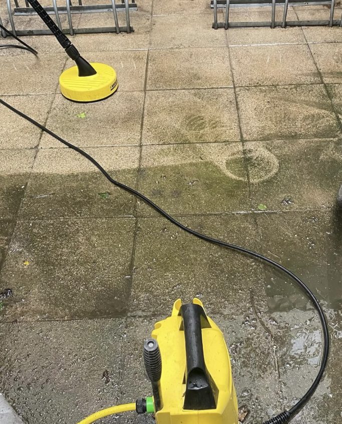 Reinigungsgerät mit gelber Basis auf einem unebenen, schmutzigen Pflasterboden.